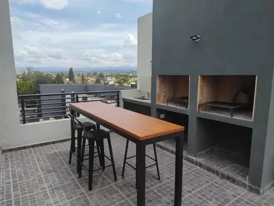 a table and chairs on a balcony with a fireplace at Dpto frente al Lago Carlos Paz in Villa Carlos Paz