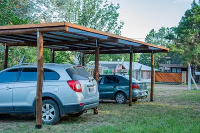two cars parked under a wooden pavilion at Complejo Montana Departamento 3 in Potrero de Garay