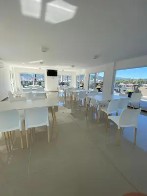 a dining room with white tables and chairs and windows at Departamento centrico en carlos paz in Villa Carlos Paz