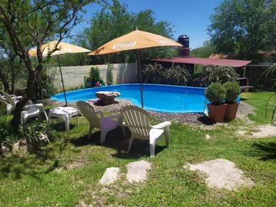 a yard with chairs and an umbrella and a pool at Monoambiente con piscina compartida in Mina Clavero
