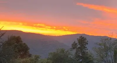 a sunset in the mountains with trees in the foreground at Ataias 2 in Santa Rosa de Calamuchita