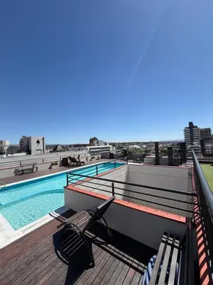 a deck with chairs and a swimming pool on a building at Depto Céntrico, Cochera, Pile, Terraza in Villa Carlos Paz