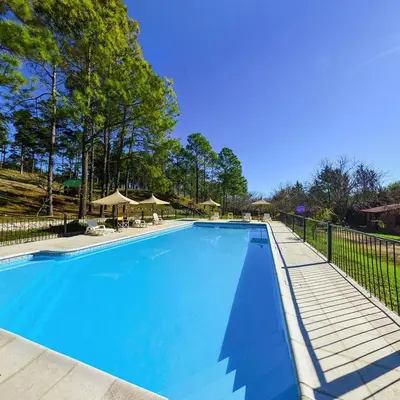a large blue swimming pool with tables and umbrellas at Pinar del Arroyito in Villa General Belgrano