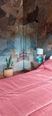 a bedroom with a red bed and a stone wall at Tierra de Sueños in Santa Rosa de Calamuchita