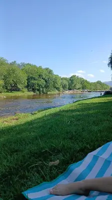 a person laying on a blanket on the grass next to a river at La Soñada in Villa Independencia